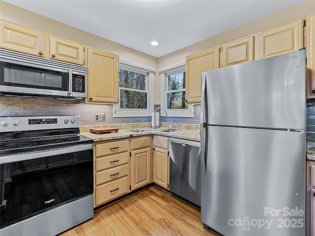 kitchen with a sink, light stone counters, appliances with stainless steel finishes, and light brown cabinetry