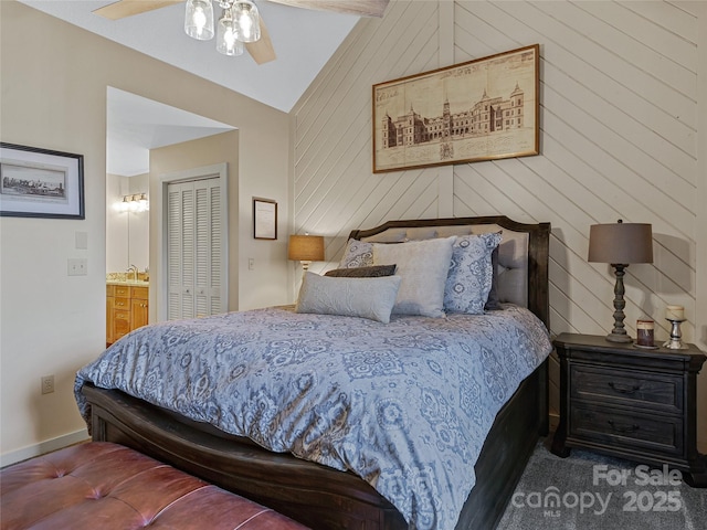 carpeted bedroom with ceiling fan, vaulted ceiling, a closet, wood walls, and connected bathroom