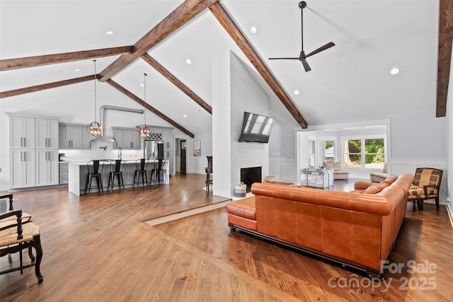 living area with ceiling fan, a fireplace, beamed ceiling, and wood finished floors