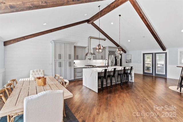 dining area with lofted ceiling with beams, dark wood-style floors, and a decorative wall