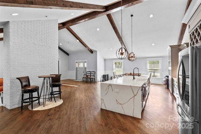 kitchen featuring wainscoting, an island with sink, light stone counters, smart refrigerator, and beam ceiling