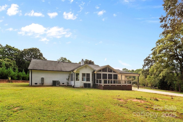 back of house with a sunroom, a chimney, cooling unit, and a lawn