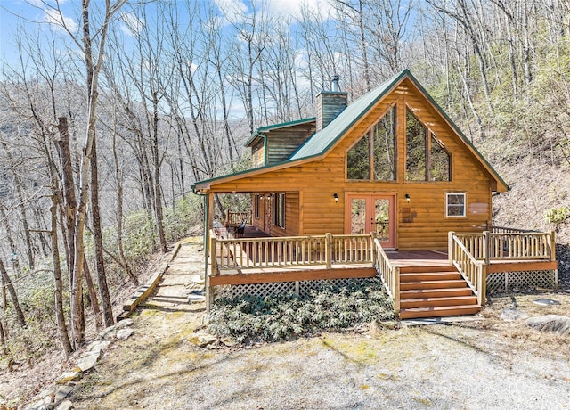 view of front of property with faux log siding, a chimney, metal roof, a deck, and french doors