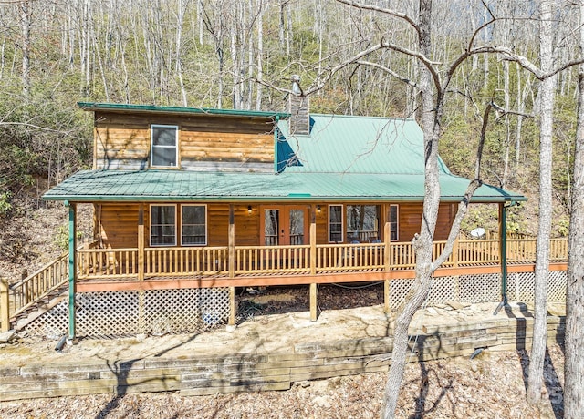 view of front of house featuring metal roof, a porch, a chimney, and a forest view