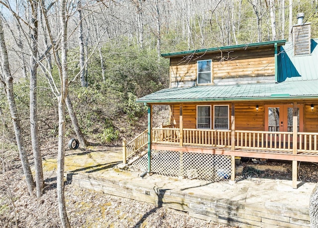 view of front of house featuring a view of trees, a chimney, metal roof, french doors, and a porch