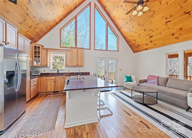 kitchen with a sink, open floor plan, french doors, stainless steel fridge with ice dispenser, and dark countertops