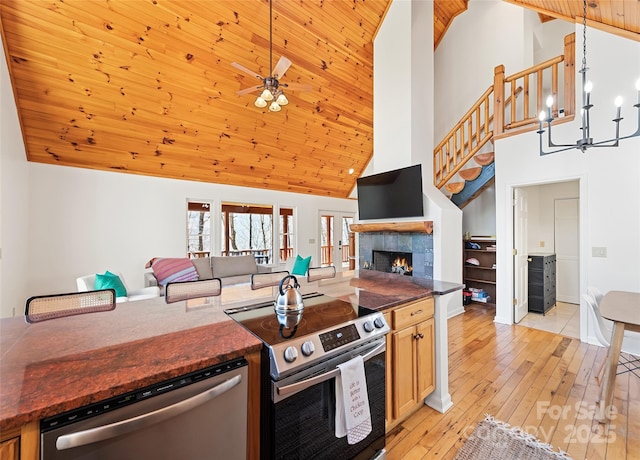 kitchen featuring a tiled fireplace, appliances with stainless steel finishes, open floor plan, light wood-style floors, and ceiling fan with notable chandelier