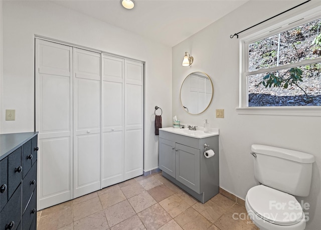 bathroom featuring toilet, baseboards, stone tile flooring, and vanity