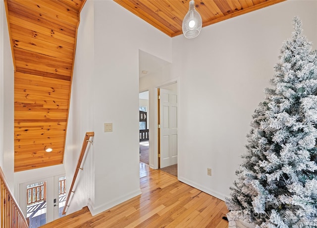 corridor with a high ceiling, wood ceiling, an upstairs landing, baseboards, and light wood finished floors