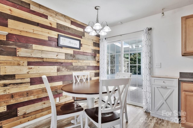 dining space featuring light wood-style flooring, wooden walls, and an inviting chandelier