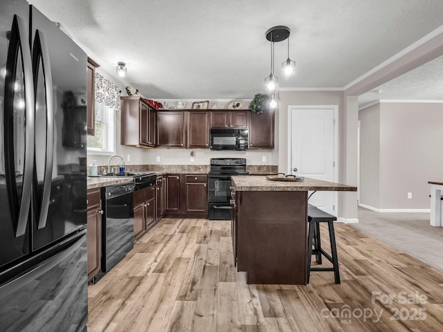 kitchen with dark brown cabinetry, ornamental molding, a breakfast bar, black appliances, and a sink