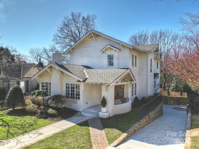 traditional home featuring brick siding, a shingled roof, a chimney, and a front yard