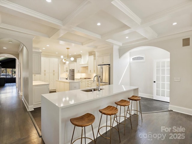 kitchen featuring arched walkways, a large island, custom range hood, appliances with stainless steel finishes, and a sink