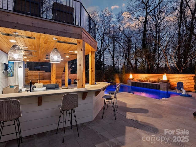 patio terrace at dusk with outdoor dry bar, ceiling fan, fence, and a fenced in pool