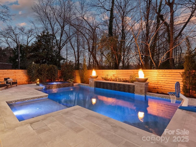 pool at dusk featuring an in ground hot tub, a patio area, a fenced backyard, and a fenced in pool