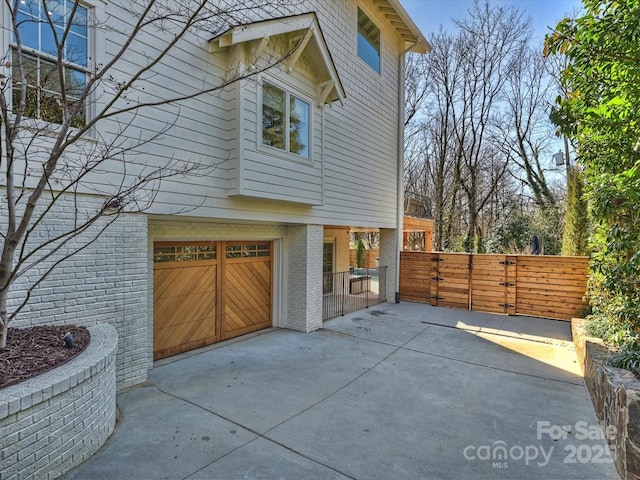 view of home's exterior with brick siding, an attached garage, a gate, fence, and driveway