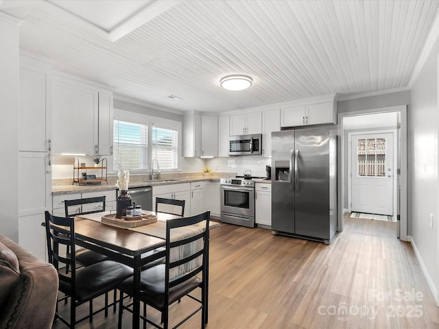 kitchen with crown molding, stainless steel appliances, white cabinets, a sink, and wood finished floors