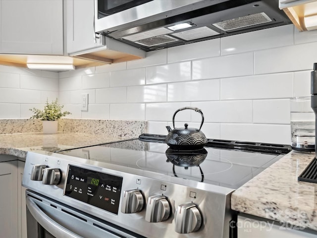 kitchen with white cabinets, decorative backsplash, stainless steel electric range oven, light stone countertops, and range hood