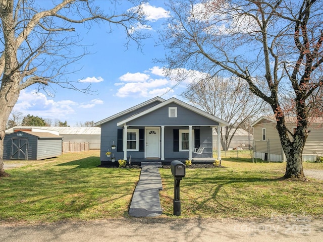 bungalow-style house with a storage unit, a front lawn, a porch, and fence