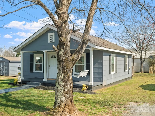 bungalow with a storage unit, a porch, fence, an outdoor structure, and a front lawn