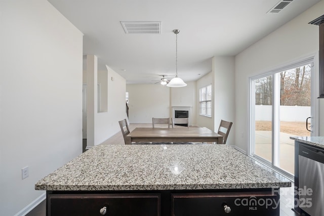 kitchen featuring visible vents, a kitchen island, light stone countertops, a glass covered fireplace, and stainless steel dishwasher