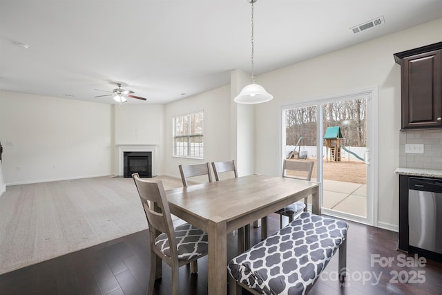 dining area featuring dark wood finished floors, visible vents, baseboards, and a fireplace with flush hearth