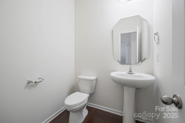 half bath featuring a sink, baseboards, toilet, and wood finished floors