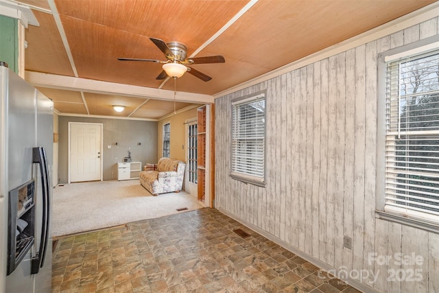 sitting room featuring ceiling fan, wood walls, stone finish flooring, wooden ceiling, and carpet flooring