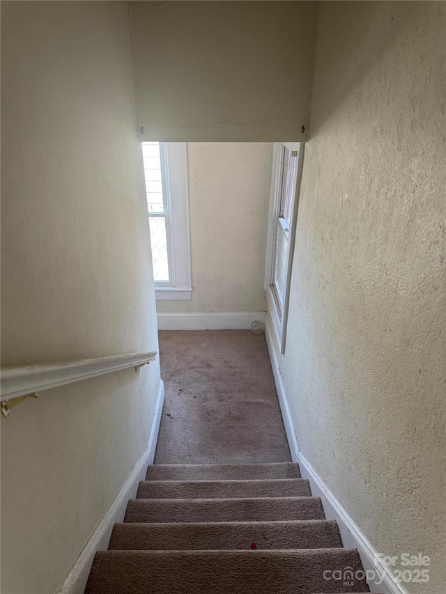 staircase featuring carpet floors, a textured wall, and baseboards