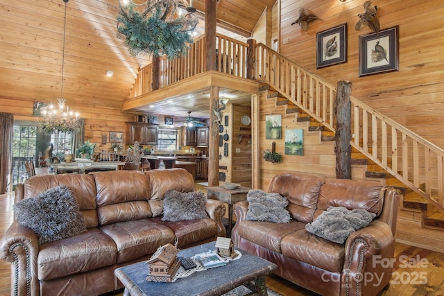 living room featuring high vaulted ceiling, wooden ceiling, ceiling fan with notable chandelier, wood walls, and stairs