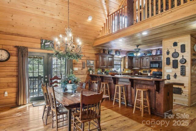 dining area featuring wooden walls, a towering ceiling, wooden ceiling, light wood-style flooring, and ceiling fan with notable chandelier