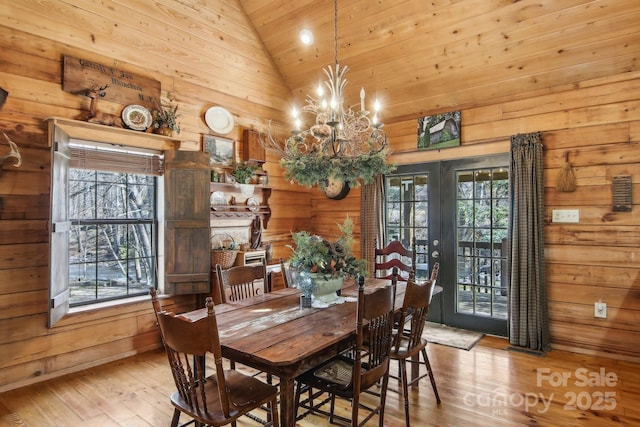 dining space with a healthy amount of sunlight, wooden walls, a chandelier, and vaulted ceiling