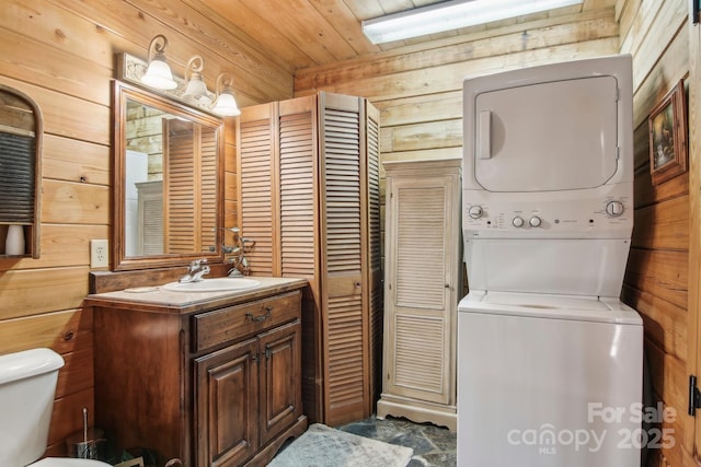 bathroom featuring wooden walls, stacked washer / dryer, toilet, wood ceiling, and vanity