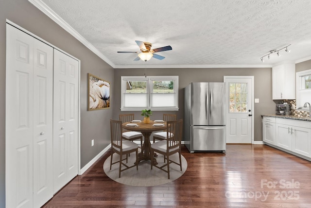 dining space featuring baseboards, dark wood finished floors, ornamental molding, a textured ceiling, and a ceiling fan