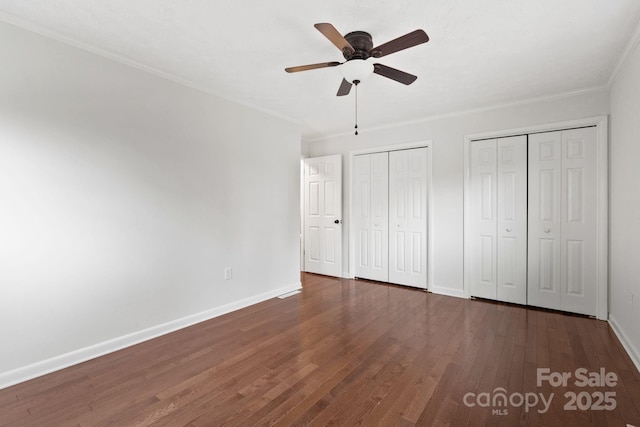 unfurnished bedroom featuring wood finished floors, baseboards, two closets, and ornamental molding