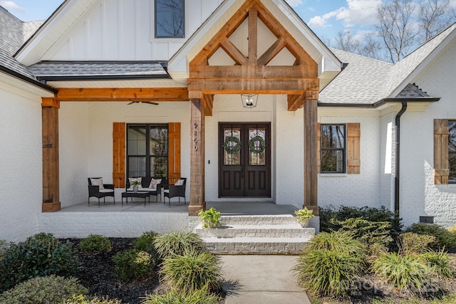 view of exterior entry with roof with shingles, a porch, and board and batten siding