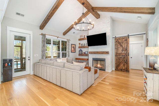 living room featuring a chandelier, a barn door, light wood-style flooring, visible vents, and beam ceiling