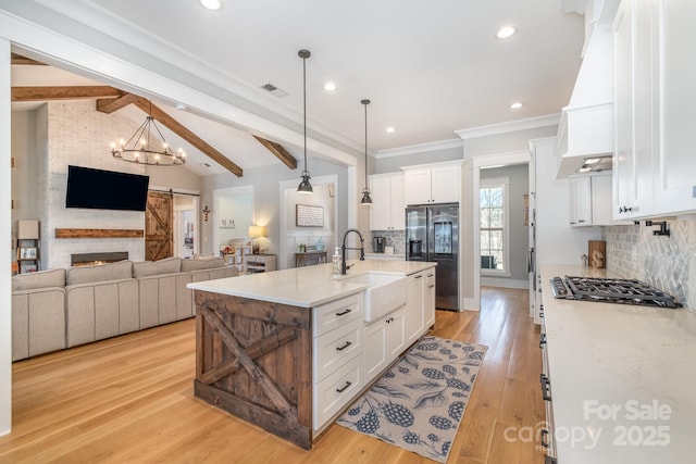 kitchen featuring vaulted ceiling with beams, stainless steel appliances, a barn door, white cabinetry, and a sink