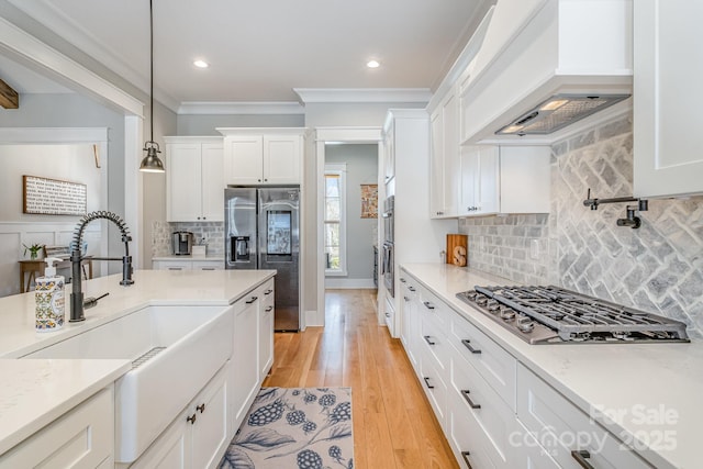 kitchen featuring a sink, white cabinetry, ornamental molding, appliances with stainless steel finishes, and custom range hood