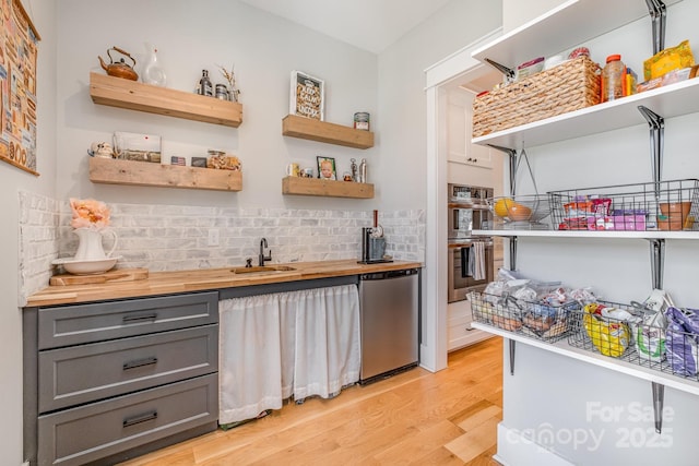 bar featuring light wood-type flooring, tasteful backsplash, stainless steel appliances, and a sink