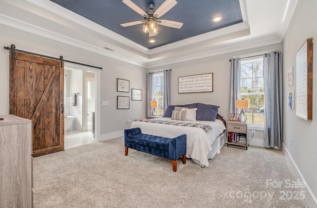 carpeted bedroom with a tray ceiling, a barn door, ornamental molding, ensuite bath, and baseboards