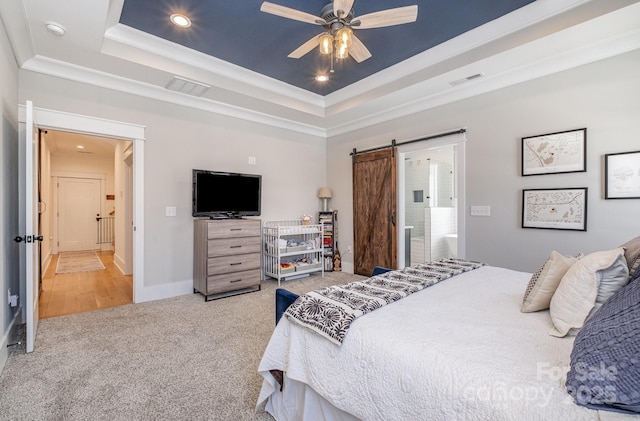 bedroom with a tray ceiling, a barn door, carpet, and visible vents