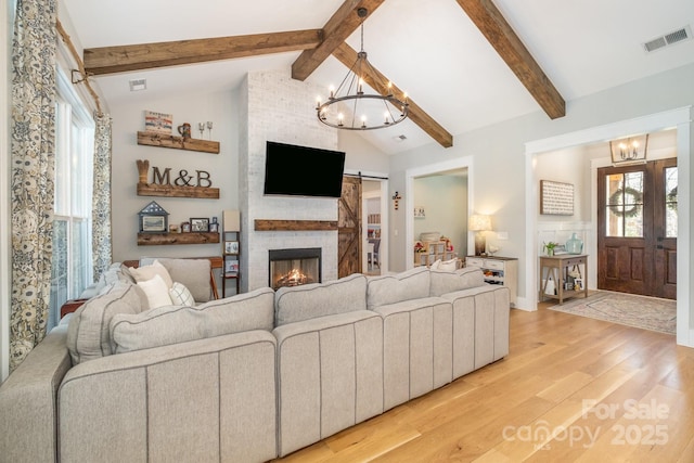 living area with visible vents, lofted ceiling with beams, an inviting chandelier, light wood-style floors, and a barn door