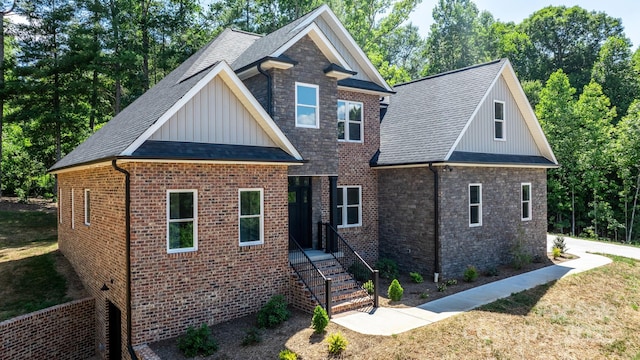 view of front of property featuring stone siding, a front yard, board and batten siding, and roof with shingles