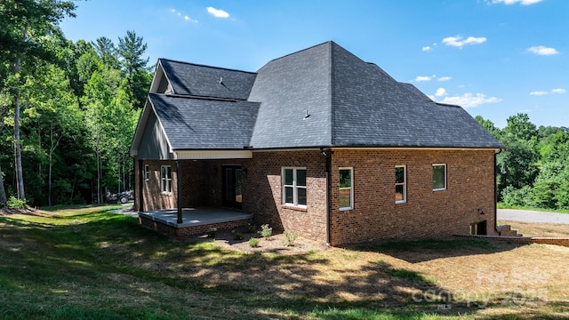 view of side of home with a yard, a shingled roof, a patio, and brick siding