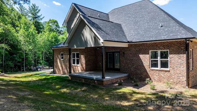 rear view of property with a yard, roof with shingles, a patio, and brick siding