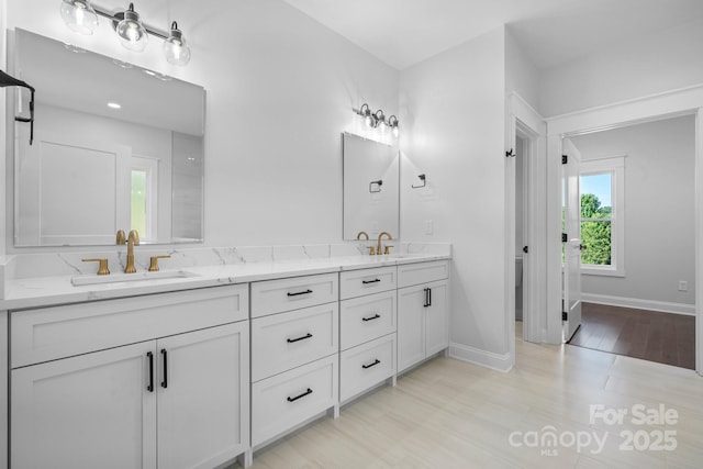 bathroom with wood finished floors, a sink, baseboards, and double vanity