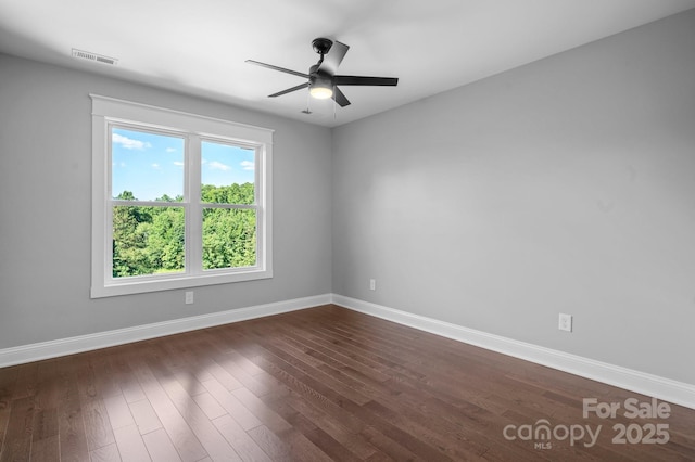 empty room featuring dark wood-style floors, a ceiling fan, visible vents, and baseboards