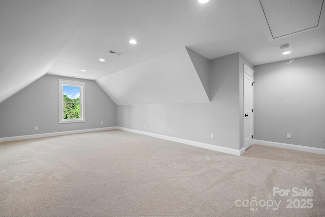 additional living space with visible vents, attic access, light carpet, vaulted ceiling, and baseboards