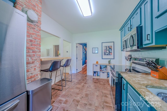 124 Dodge St, Asheville, NC 28803 - kitchen featuring appliances with stainless steel finishes, brick patterned floors, blue cabinetry, and a breakfast bar